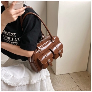 Detailed close-up of glossy brown shoulder bag featuring dual front buckle pockets