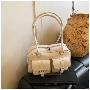Detail of cream shoulder bag with dual front pockets and silver buckles on an art book