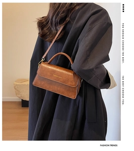 Sac vintage marron à rabat avec détails dorés porté en bandoulière par un mannequin chic