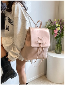 Detail eines hellrosa Lederrucksacks mit Schleifendekor und Schultergurt aus Metallkette