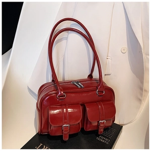 Macro shot of dark red glossy leather shoulder bag featuring silver hardware and pockets