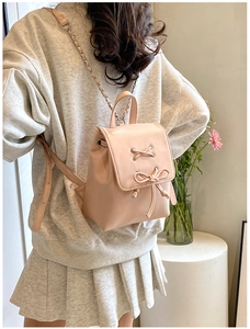Details eines hellen apricotfarbenen Rucksacks mit Schleife und Kettenriemen am Modell