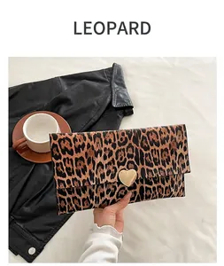 Détail d'une pochette léopard avec fermoir coeur doré tenue à la main par un mannequin