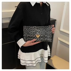 Détail d'une pochette léopard gris avec boucle coeur dorée tenue par un mannequin