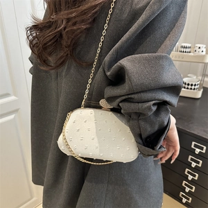 White semi-circular evening bag with 3D dot texture and gold chain worn as shoulder bag