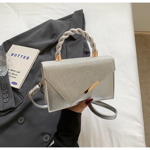 Detail of silver crossbody bag with rhinestone flap and woven metal handle on white linen