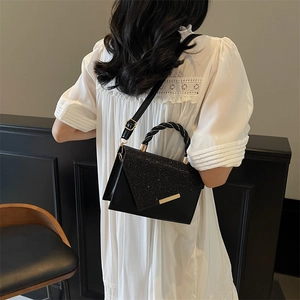 Chic black leather handbag with shimmering sequins and gold chain handle on white dress