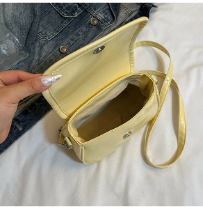 Close-up of light yellow patent leather crossbody bag with magnetic closure and lining