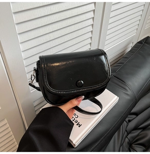 Detail shot of a black glossy saddle bag featuring a round snap closure and metallic hooks