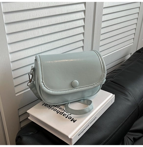 Detail of light blue vintage shoulder bag with round buckle on white decorative books