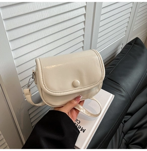 Detail of creamy white crossbody bag showing glossy faux leather texture and round buckle