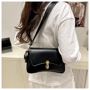 Detail view of the sleek black underarm bag featuring a metallic gold capsule twist lock