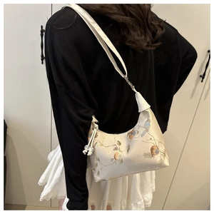 Close-up of beige silk underarm bag with bird embroidery and pearl bead drawstring detail