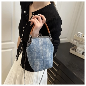 Detail of vintage denim bucket bag with metal clasp and leather handle on a model