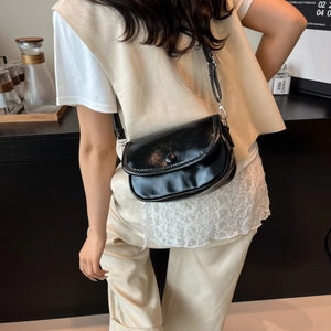 Minimalist black glossy shoulder bag with adjustable strap shown in a modern cafe setting