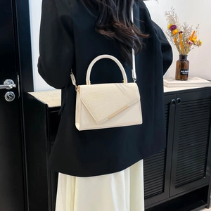 Minimalist cream-white crossbody bag with asymmetric gold trim and woven flap detail