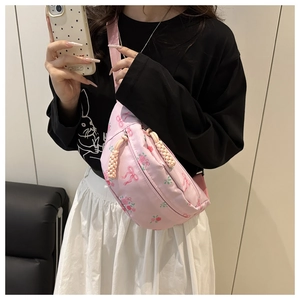 Detail of floral pink crossbody bag showing rose print and woven zipper pull on a model