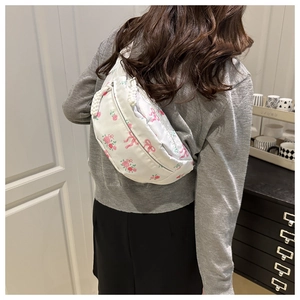 Detail of white crescent crossbody bag with pink floral patterns and woven zipper pull