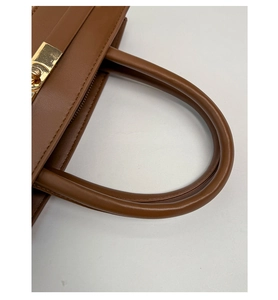 Detail einer braunen Ledertasche mit rundem Griff und goldenem Drehverschluss aus Metall