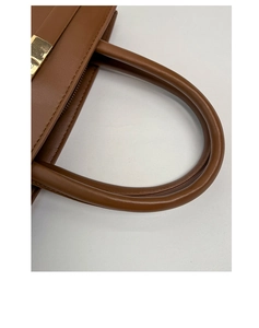 Detailaufnahme einer braunen Ledertasche mit goldenem Metallverschluss und Tragegriff