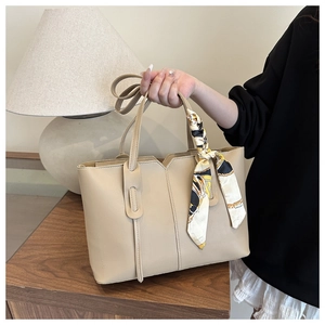 Detail of beige leather tote bag featuring an elegant patterned silk scarf handle wrap