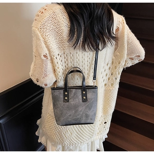 Détail du sac seau vintage gris avec bandoulière noire et rivets sur escalier en bois