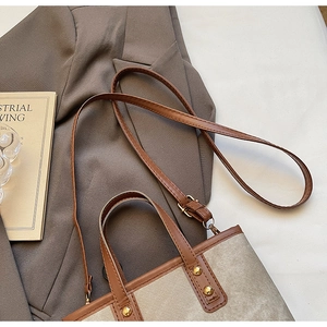 Détail du sac cabas en toile avec garniture en cuir brun et clous dorés sur un blazer
