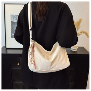 Dettaglio borsa a mezzaluna bianca con nappa intrecciata colorata su blazer nero