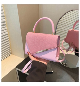 Pink handbag with woven texture flap and gold metallic detail held by a model