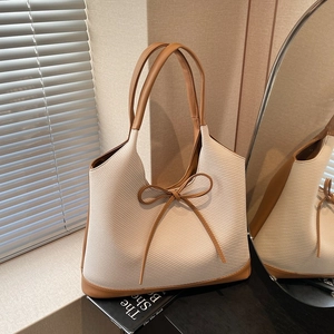 Minimalist beige woven tote bag with brown leather bow and handles shown in a warm setting