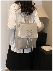 Silberner Rucksack aus glänzendem Leder mit dekorativer Schleife und eleganter Metallkette