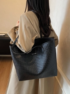Large black woven tote bag with shoulder straps in a minimalist fashion style