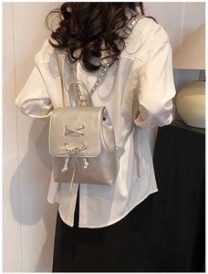 Details eines silbernen Metallic-Minirucksacks mit Schleife und Kettenriemen am Model