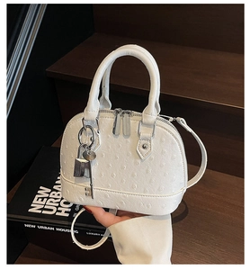 Detailansicht der weißen Schalenhandtasche mit Straußenmuster und Metallschloss-Anhänger
