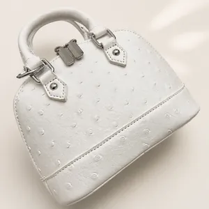 Detailansicht der weißen Muscheltasche mit Straußenprägung, Doppelreißverschluss und Griff
