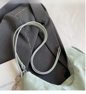 Detail of mint green half-moon tote bag with metallic buckles on a grey blazer background