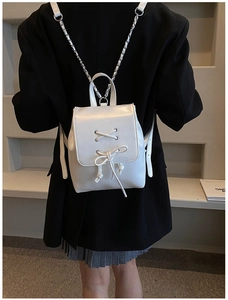 Detail eines weißen PU-Rucksacks mit Schnürschleife und Kettenriemen vor schwarzem Blazer