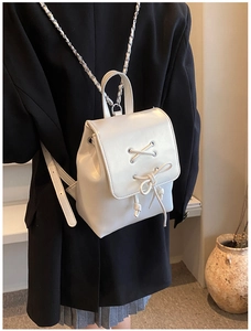 Mini-Rucksack in Perlweiß mit dekorativer Schleife und eleganten Kettenriemen am Modell
