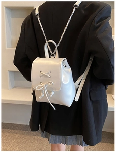Detail eines perlweißen Mini-Rucksacks mit schicker Schnürschleife und silbernen Ketten