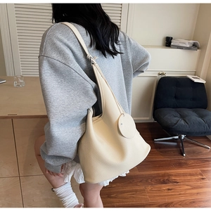 Detail view of cream lychee texture leather bucket bag with a round charm pendant
