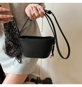 Detail van zwarte bucket bag met litchi-textuur, zilveren hartje en ritssluiting