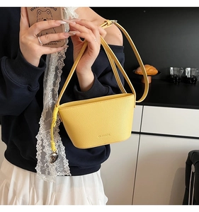 Detail van gele emmer tas in leer met litchi-textuur en metalen hart hanger