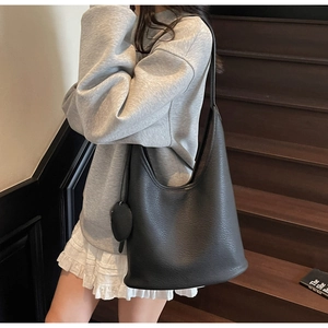 Close-up of black lychee grain bucket bag with charm shown on shoulder for daily commute