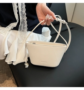 Detail van witte bucket bag van generfd leer met CLEAROK-logo en zilveren hanger bedeltje