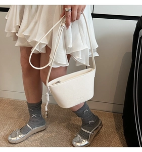 Detailopname van witte bucket bag van leer met kiezelmotief en riem op een model