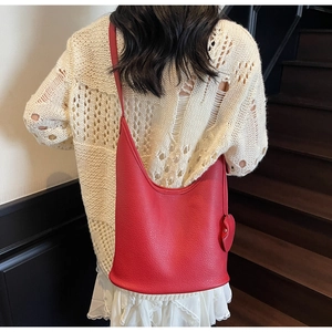 Close-up of red lychee grain leather bucket bag with heart pendant on shoulder