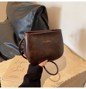 Dettaglio della borsa a tracolla in PU marrone scuro con logo dorato su pelle martellata