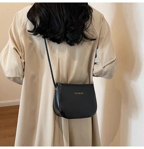 Dettaglio della borsa in pelle PU nera con logo YUSHAN dorato su cappotto beige