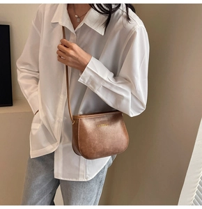 Dettaglio della borsa a sella in pelle PU marrone retrò con logo dorato su outfit bianco