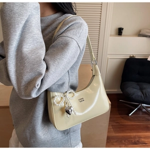 Detail of cream yellow leather bag with pearl bow, silver heart charm and metal logo